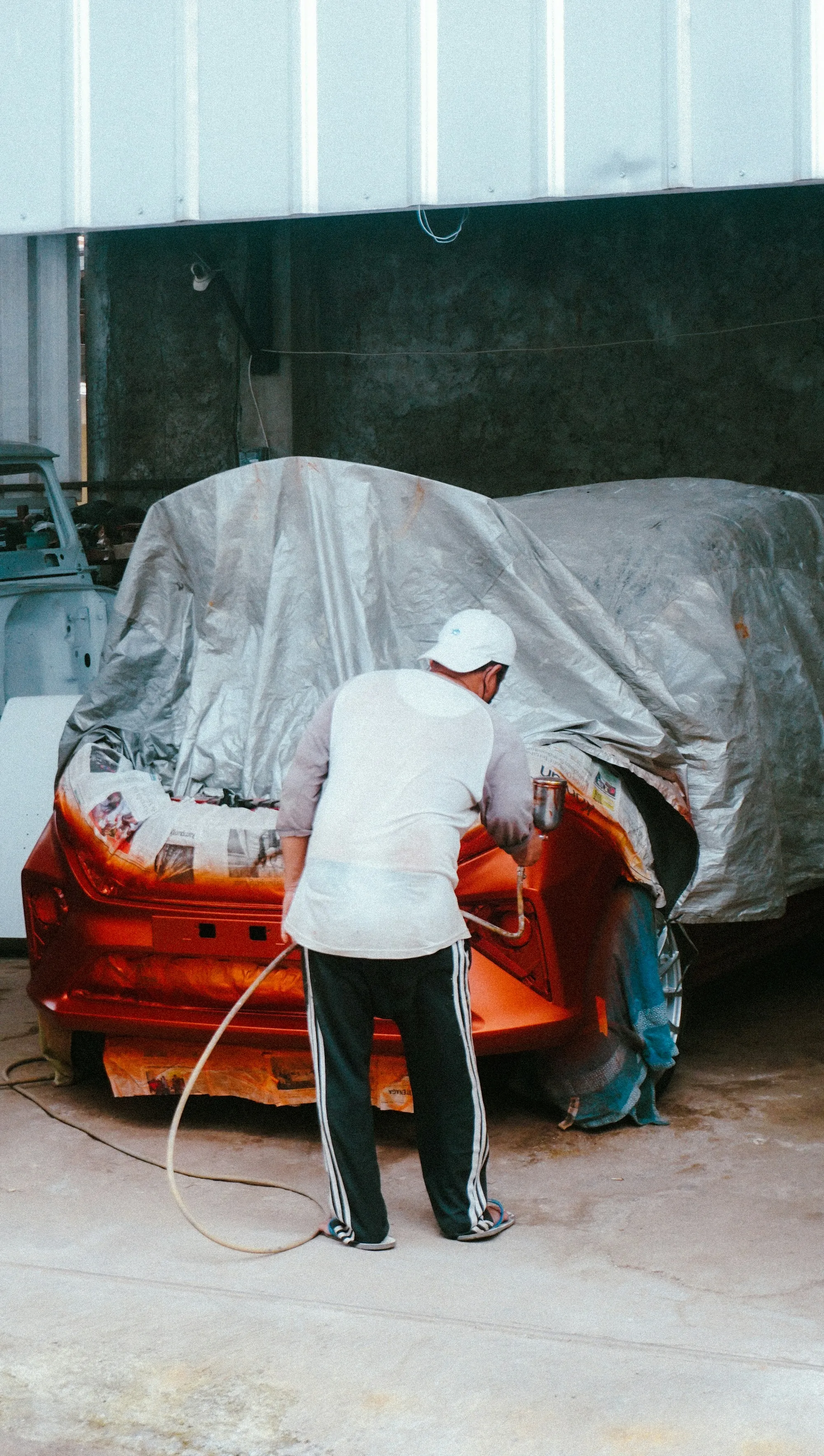 Technician working on a car under plastic sheeting in a prep area