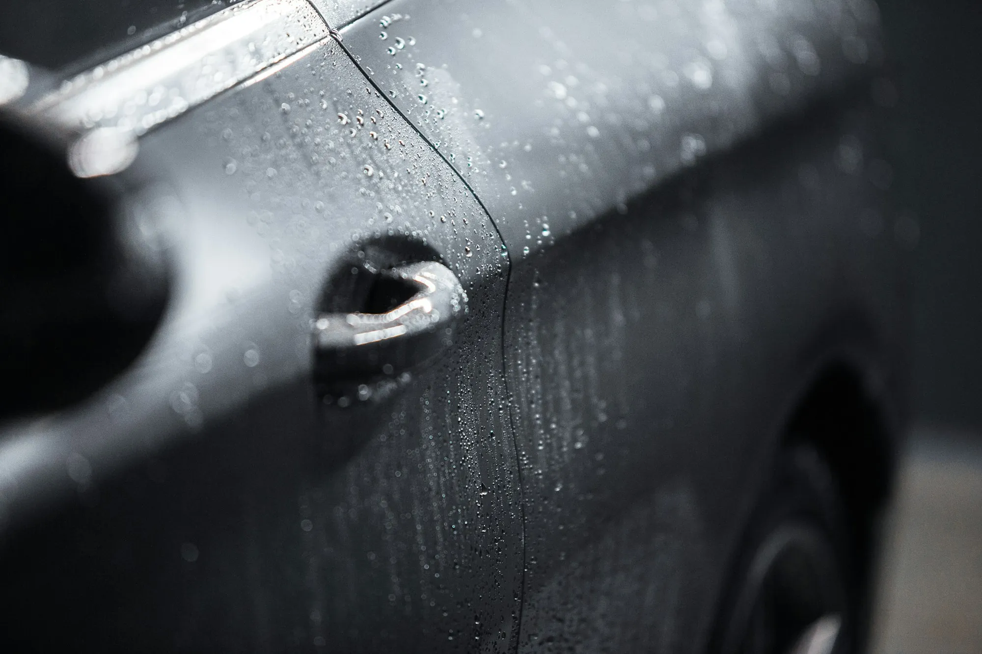 Water beaded on the door and handle of a dark car